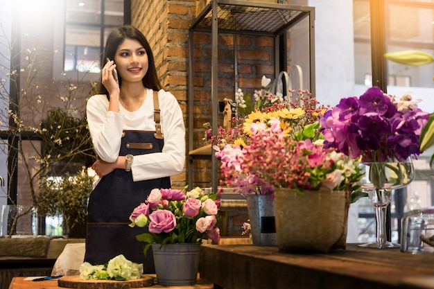 Foto florista de pie en su floristería y usando su teléfono para recibir pedidos de su tienda