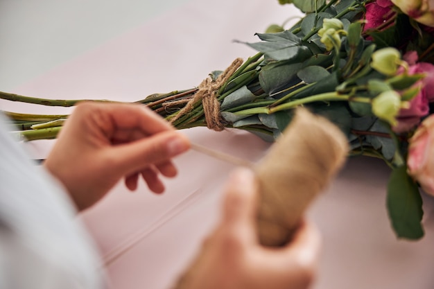 Florista qualificada preparando linha marrom para amarrar flores