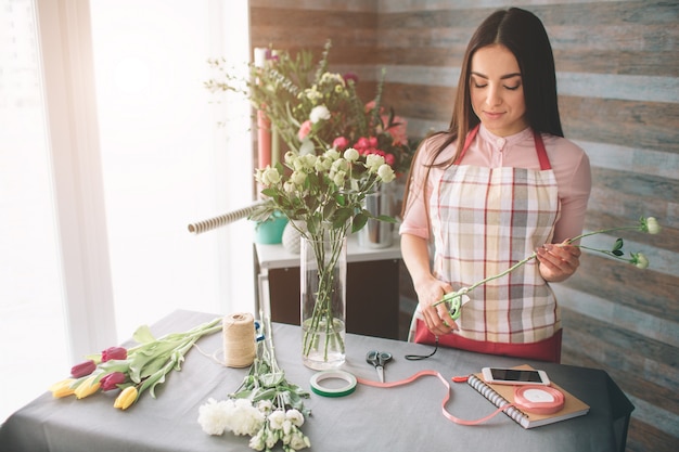 Florista de sexo femenino en el trabajo: bastante joven mujer morena haciendo moda moderno ramo de flores diferentes. Mujeres trabajando con flores en taller