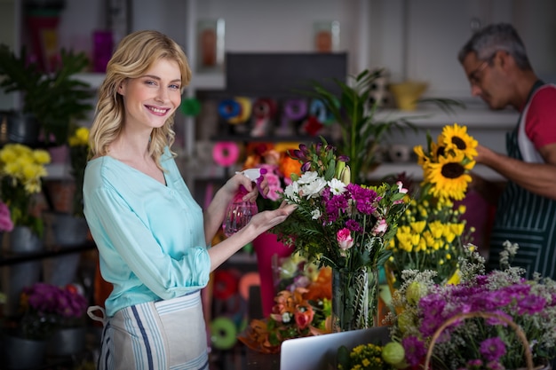 Florista sorridente pulverizando água em flores na loja de flores