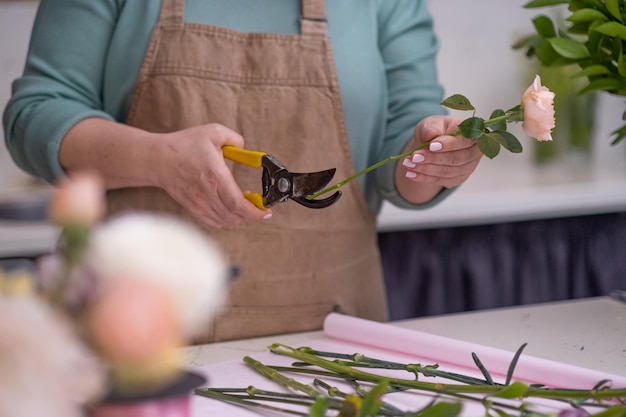 Florista talentosa en delantal eligiendo flores y hojas elaborando exquisitos ramos en floristería