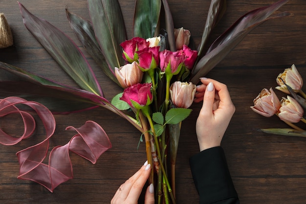 Florista trabalhando, mulher fazendo buquê moderno de flores diferentes na superfície de madeira