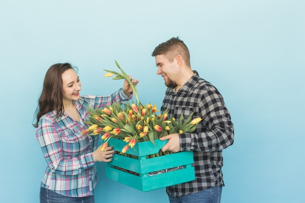 Floristas felizes consertando tulipas em uma grande caixa de madeira em azul.