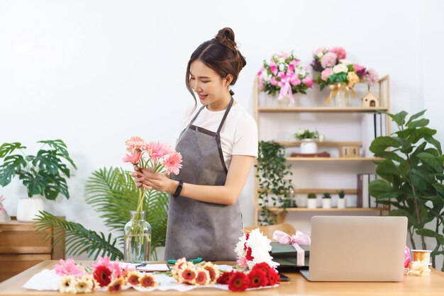 Floristenkonzept Weibliche Floristin arrangiert rosa Gerbera in Vase mit Glück im Blumenladen