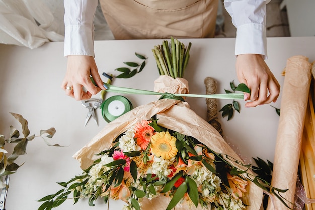 Una floristería ata un lazo de cinta en un ramo de flores envueltas en papel artesanal en el escritorio