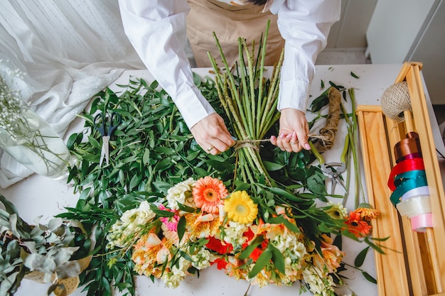 Una floristería ata un ramo de flores frescas con un cordel en su escritorio lleno de hojas cortadas