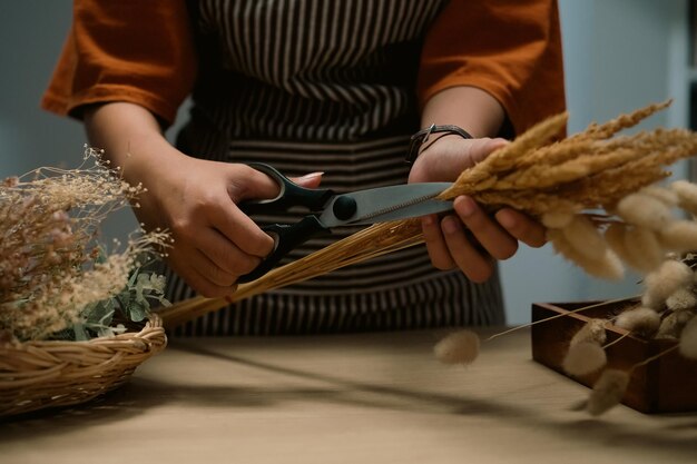 Floristería con delantal cortando con tijeras arreglando un ramo de flores secas en su taller