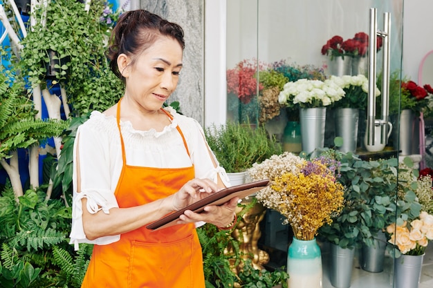 Floristería femenina asiática senior comprobando los pedidos de los clientes en la computadora de la tableta