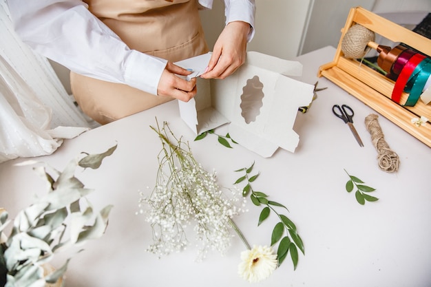 Floristería femenina hace una caja de regalo de papel blanco en su escritorio en una tienda de flores