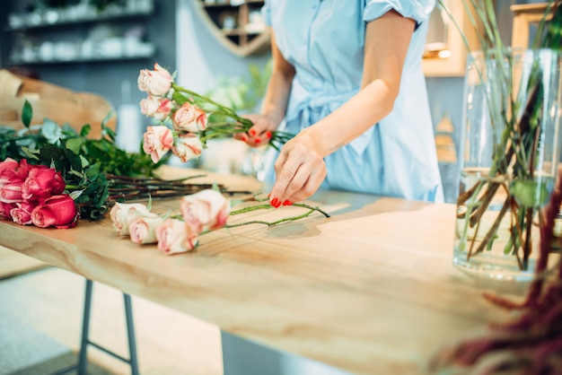 Floristería femenina hace composición rosa sobre la mesa en la florería. Artista floral haciendo ramo en el lugar de trabajo