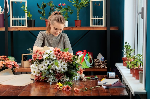 Floristería hace un ramo de crisantemos multicolores. Una joven adulta trabaja con entusiasmo.