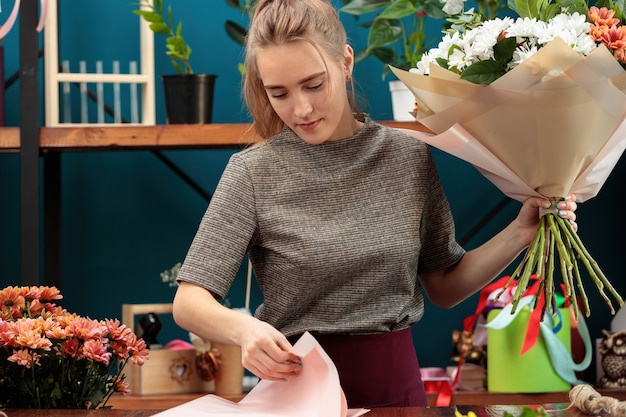 Floristería hace un ramo. Una joven adulta sostiene un gran ramo de crisantemos multicolores en sus manos y elige papel para decorar.