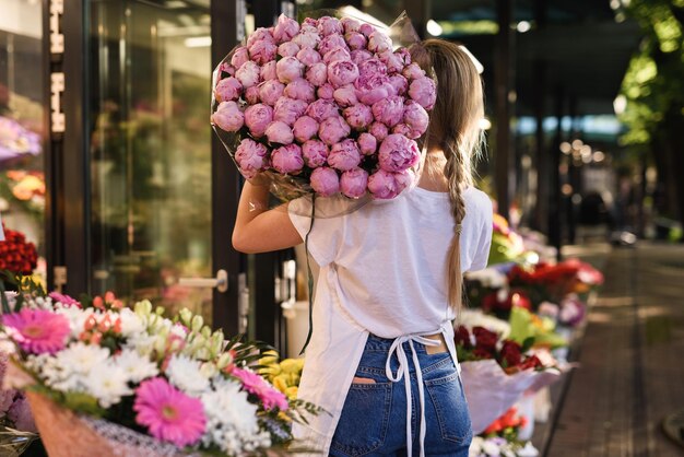 Floristería joven con un montón de flores de peonía rosa en su pequeña florería
