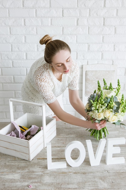 Floristería mostrar ramo de flores en la tienda. Niña propone comprar un ramo nupcial de flores blancas en un taller. Estudio de decorador de luz con pared de ladrillo en el fondo.