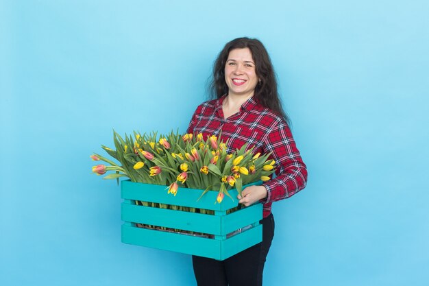 Floristería mujer caucásica feliz riendo y sosteniendo una gran caja de tulipanes en azul