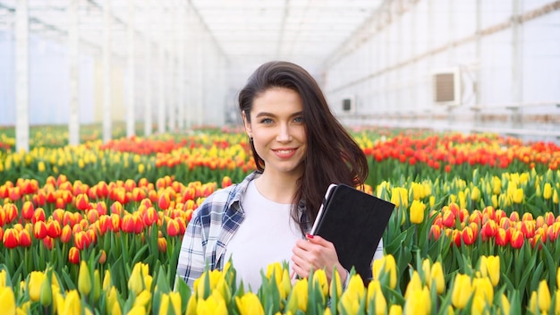 Floristería mujer sonriente joven está de pie con una tableta en sus manos en un invernadero