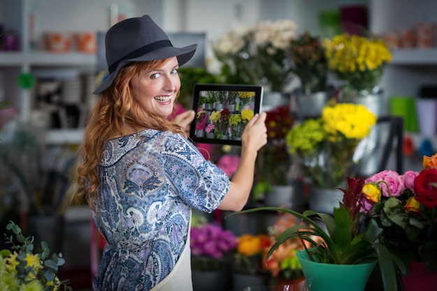 Floristería mujer tomando fotografía de flores de tableta digital en florería