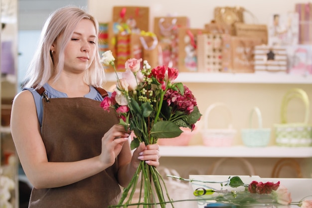 Floristería rubia en delantal en el espacio de trabajo de la florería. Enfoque selectivo.