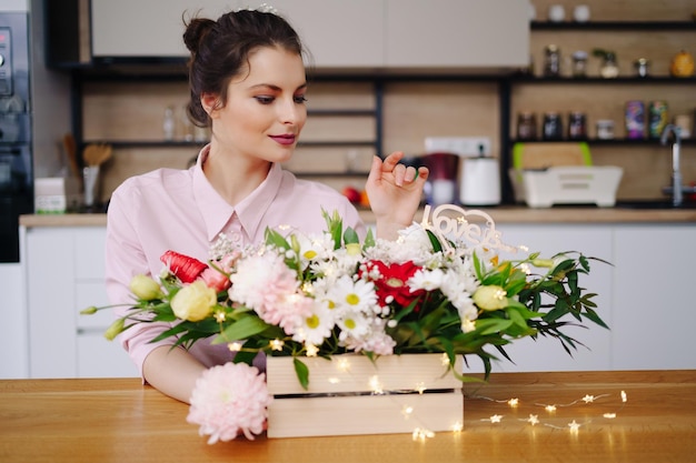 Floristería en el trabajo bastante joven mujer morena haciendo composición moderna de moda de diferentes flores decorando con luces led en casa