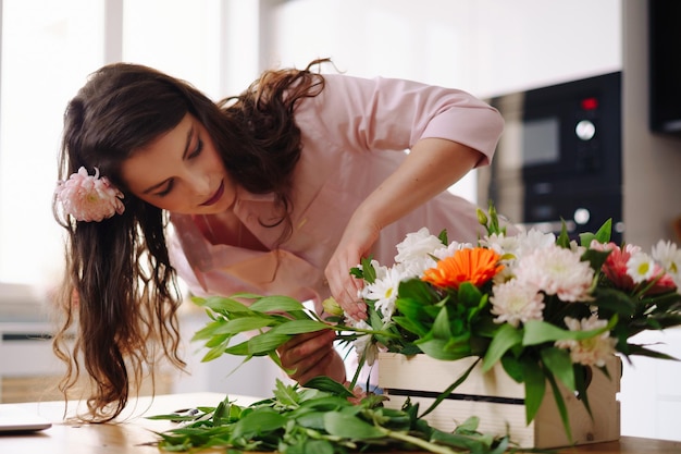 Floristin bei der Arbeit hübsche junge brünette Frau, die zu Hause eine moderne Komposition aus verschiedenen Blumen macht