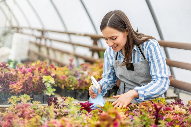 Floristin in Schürze Wasserblumen Plantage verwenden Gießkanne lächelnd genießen Pflanzenanbau