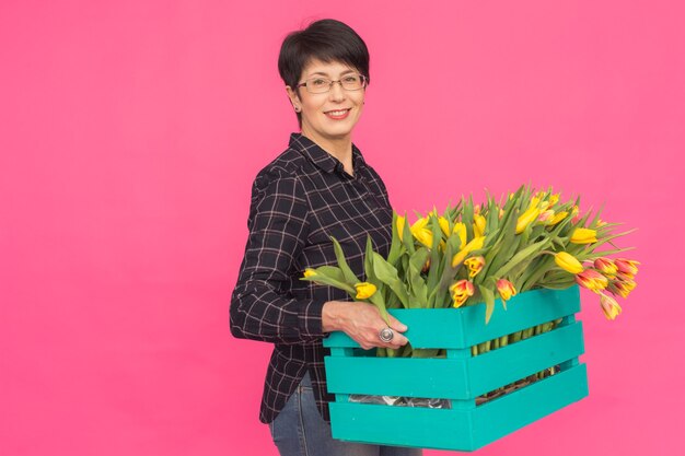 Floristin mittleren Alters, die blaue hölzerne Tulpenschachtel in rosa Oberfläche hält