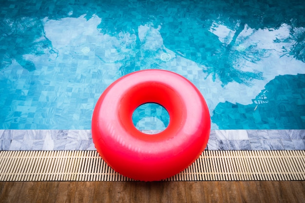 Flotador rojo de la piscina, anillo que flota en una refrescante piscina azul con sombra de árbol de coco.