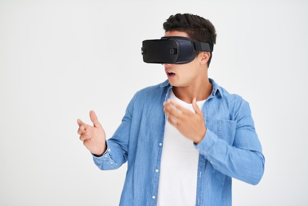 Flucht in den Cyberspace Studioaufnahme eines jungen Mannes, der erstaunt aussieht, während er ein VR-Headset vor einem weißen Hintergrund trägt