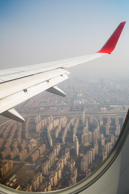 Flügel eines Flugzeuges, das über die Wolken fliegt. Menschen schauen aus dem Fenster des Flugzeugs in den Himmel