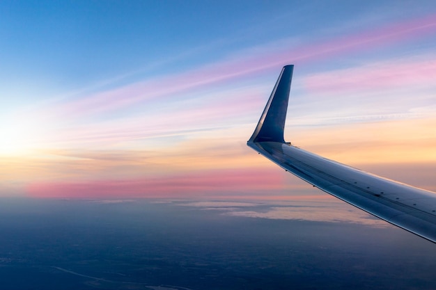 Flügel eines Flugzeugs aus dem Fenster bei Sonnenuntergang. Sonniger bunter Himmelshintergrund.