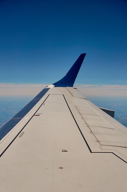 Flügel eines Flugzeugs, das über die Wolken und grünen Felder fliegt