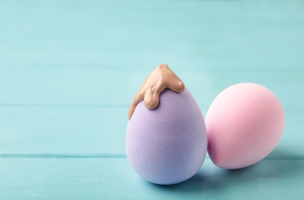 Flüssige beige Make-up-Grundlage auf neuen lila Schwämmen auf blauem Hintergrund