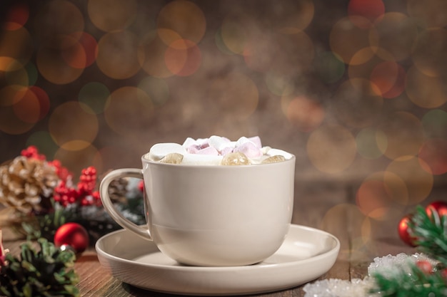 Flüssige heiße Schokolade mit Marshmallows im Becher, unscharfer Bokeh-Hintergrund, Weihnachtstasse auf Holzhintergrund, verziert mit Tannenzweigen und Weihnachtskugel, Neujahrsfeierkonzept