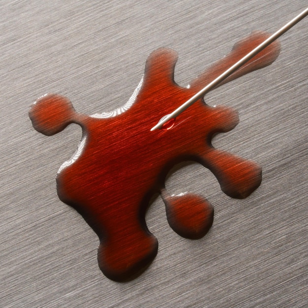 Flüssiger blutiger Fleck auf einer mit Metalloberfläche lackierten Nadel