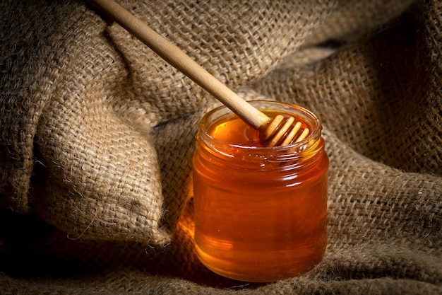 Flüssiger Honig mit einem Honiglöffel in einem Glasgefäß auf Sackleinen Nahaufnahme Seitenansicht