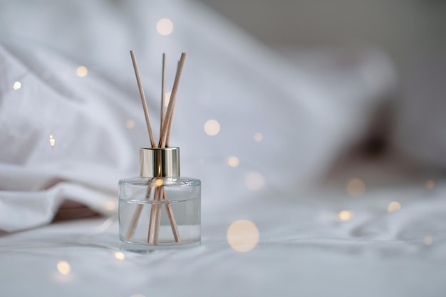 Flüssiges Parfüm für Zuhause in Glasflasche mit Bambusstöcken über leuchtenden Lichtern, Nahaufnahme Aromatherapie