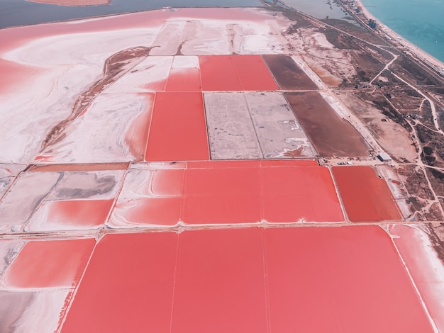 Flug über einen rosa Salzsee Salzproduktionsanlagen Salzverdunstungsteichfelder im Salzsee Dunaliella salina verleihen einem Mineralsee mit trockener kristallisierter Salzküste ein rotrosa Wasser