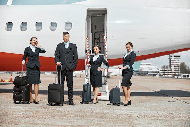 Flugbegleiter und Stewardessen stehen auf der Landebahn in der Nähe des Flugzeugjets. Modernes Passagierflugzeug. Mann und Frau mit Gepäck tragen Uniform. Zusammenarbeit. Zivile kommerzielle Luftfahrt. Flugreisekonzept