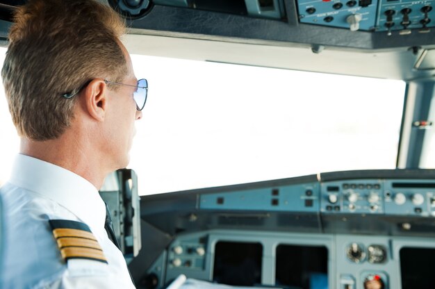 Flugfertig machen. Rückansicht eines selbstbewussten männlichen Piloten, der im Flugzeugcockpit sitzt