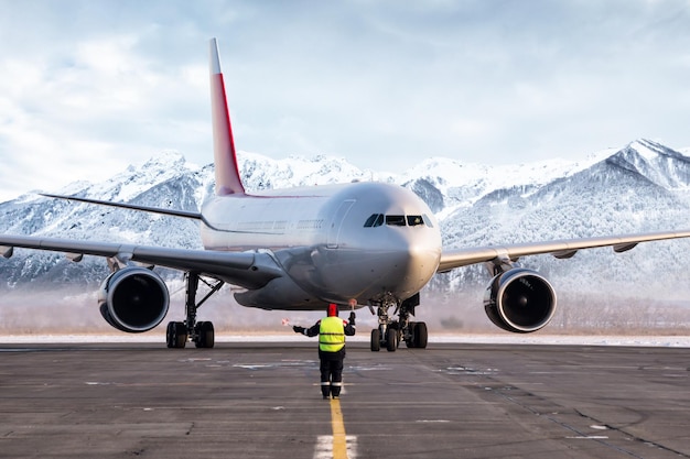 Flughafenbeauftragter trifft Passagierflugzeug auf dem Hintergrund hoher malerischer Berge