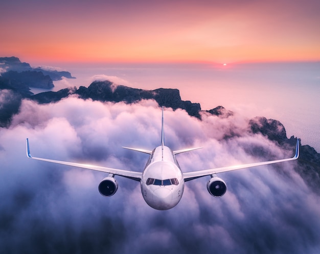Flugzeug fliegt über Wolken bei Sonnenuntergang im Sommer. Landschaft mit Passagierflugzeug, niedrigen Wolken, Meer, lila Himmel in der Dämmerung