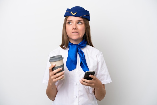 Flugzeug litauische Stewardess isoliert auf weißem Hintergrund mit Kaffee zum Mitnehmen und einem Handy, während sie etwas denkt