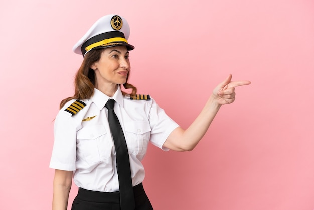 Flugzeug Pilotin mittleren Alters isoliert auf rosa Hintergrund wegweisend