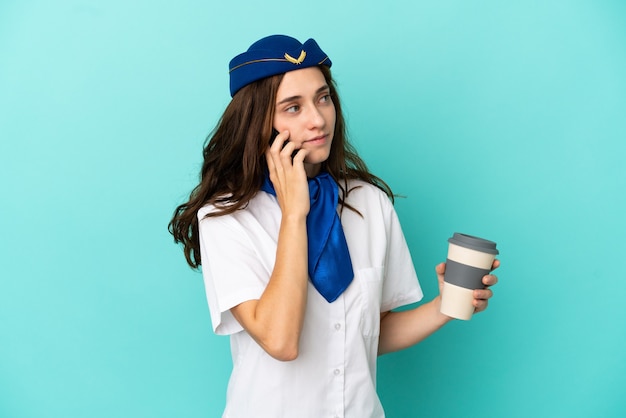 Flugzeug-Stewardess-Frau isoliert auf blauem Hintergrund mit Kaffee zum Mitnehmen und einem Handy