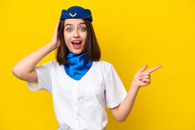 Flugzeug Stewardess ukrainische Frau isoliert auf gelbem Hintergrund überrascht und zeigt mit dem Finger zur Seite