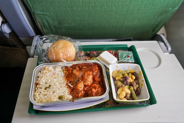 Flugzeugessen, Reis und Hühnerfleisch mit Bohnensalat, auf einem Tabletttisch