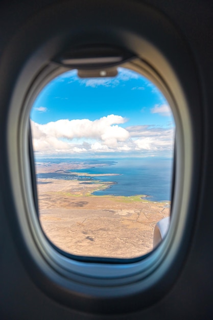 Flugzeugfensterrahmenansicht, die an einem sonnigen Tag über Land und Meer fliegt