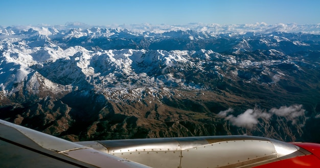 Flugzeugflügel über Bergdecke mit weißem Schnee. Landschaft des Berges. Blick aus dem Flugzeugfenster. Luftbild vom Flugzeug Blaue schneebedeckte Berglandschaft im Winter.