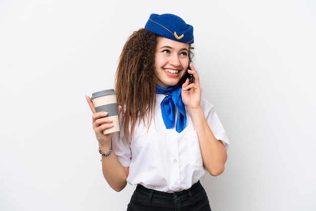 Flugzeugstewardess Arabische Frau isoliert auf weißem Hintergrund mit Kaffee zum Mitnehmen und einem Handy