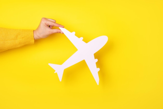 Flugzeugsymbol in der Hand über gelbem Hintergrund, Geschäftsreisekonzept